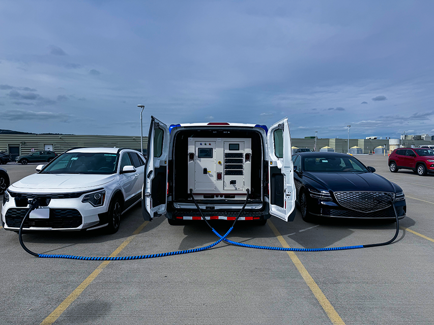 Two EVs are being charged by the PowerOnTheGo in a large outdoor parking lot.