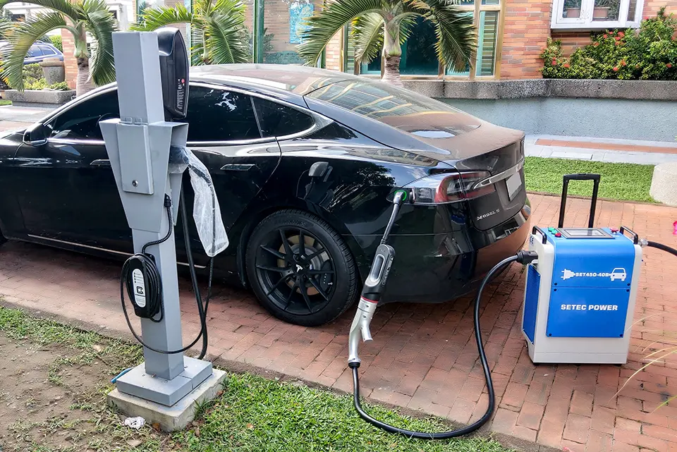 A black vehicle being charged with portable DC charger connected via an adapter